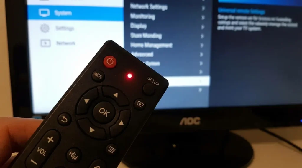 Universal remote control with LED indicator pointing at AOC television during programming setup