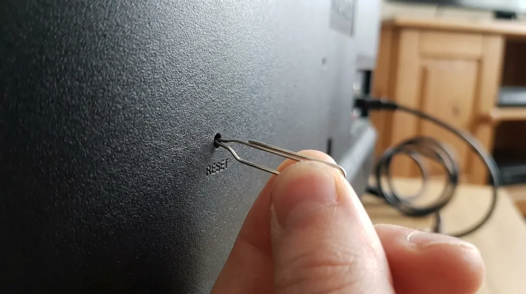 Using a paperclip to press the factory reset button on the back of an RCA TV